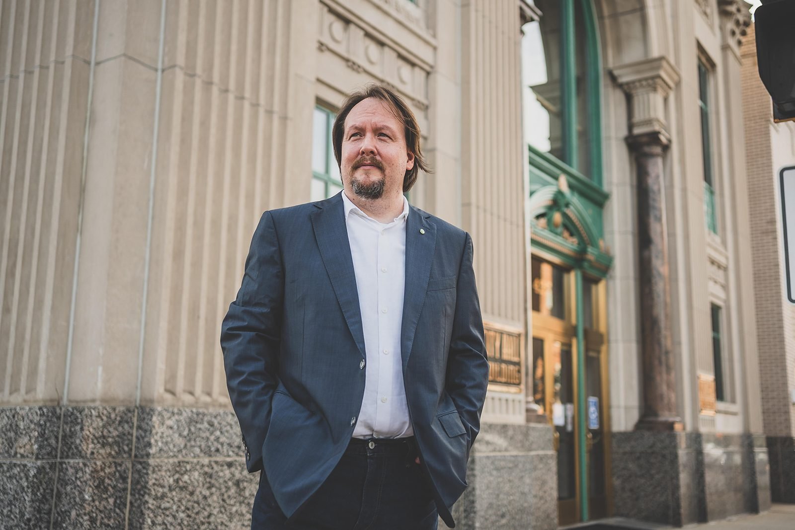Bob Blosser standing on the sidewalk outside the Rockford City Hall building, hands in his jacket pockets, looking up the street.