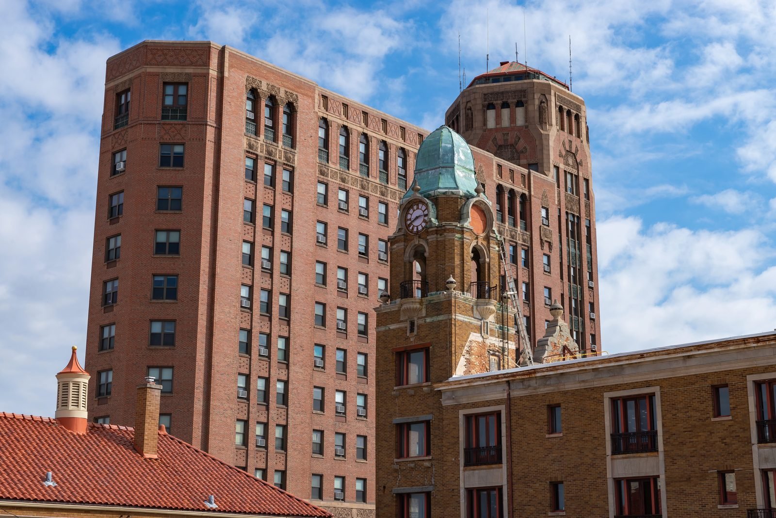 A downtown Rockford block seen from above the rooftops: a tall brick tower with terracotta detailing, a green copper clock tower in front of it, and tiled roofs below.