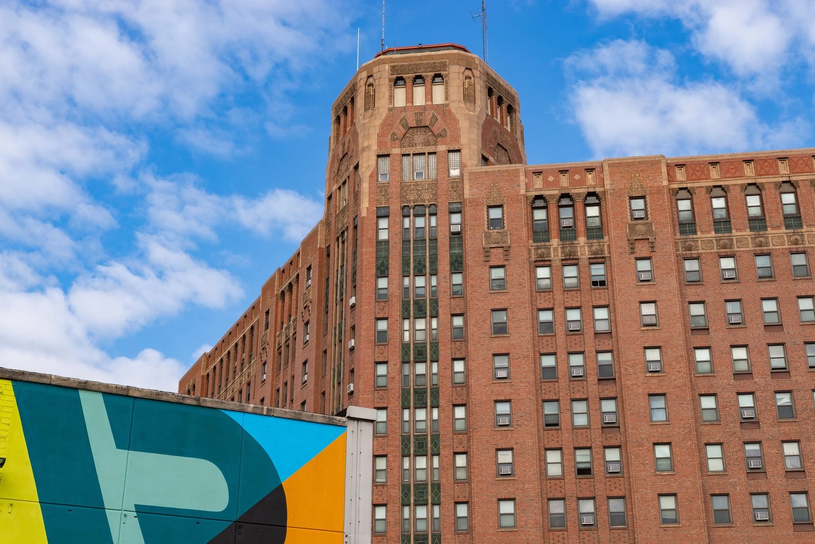 A tall brick tower in downtown Rockford with terracotta ornament and an octagonal cap, a brightly painted mural on the lower building beside it.