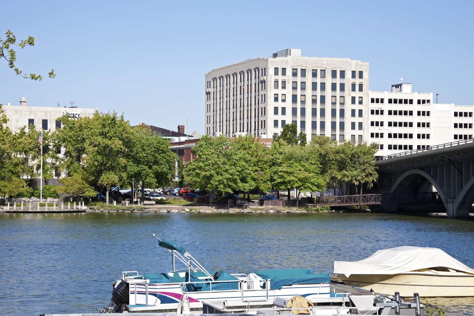 The Rock River downtown on a clear morning, with the public library, office buildings and a bridge on the far bank and boats moored in the foreground.